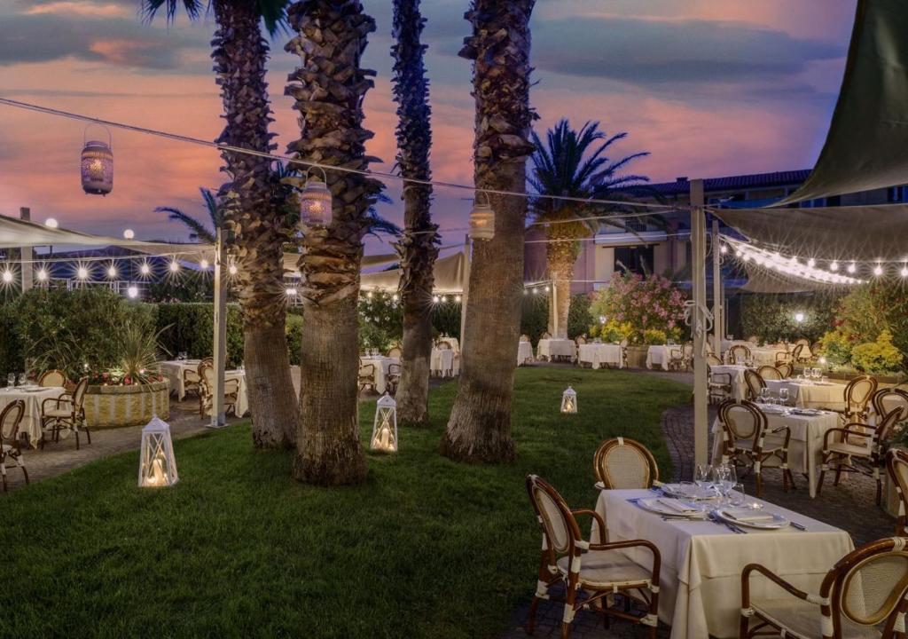 un espace repas extérieur avec tables, chaises et palmiers dans l'établissement Grand Hotel Continental, à Tirrenia