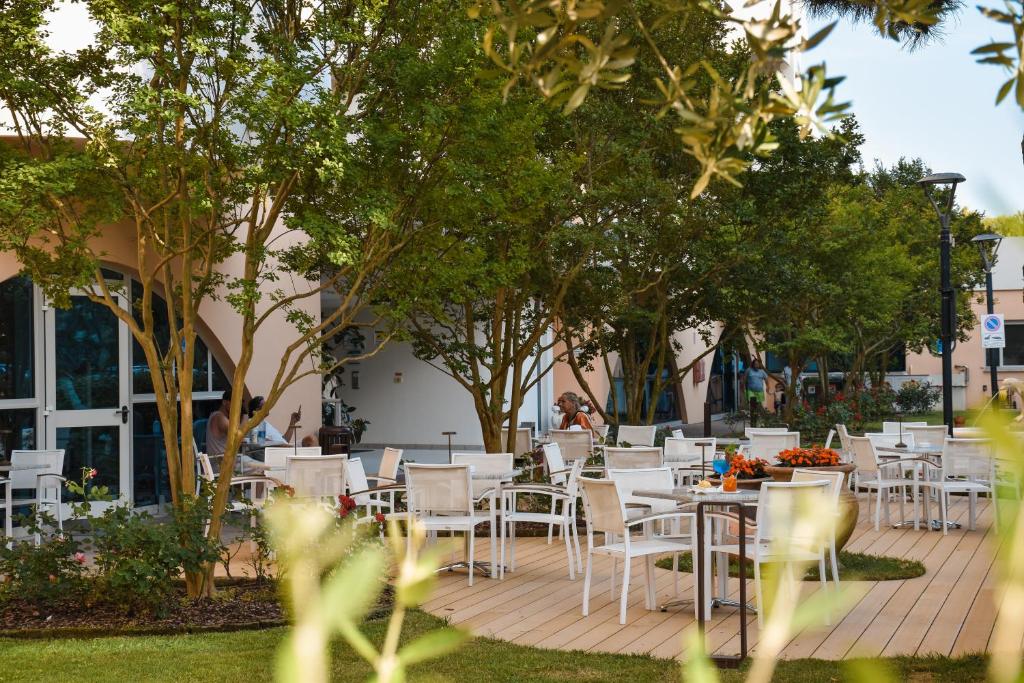 un groupe de tables avec des chaises blanches et des arbres dans l'établissement Aparthotel Holiday, à Bibione