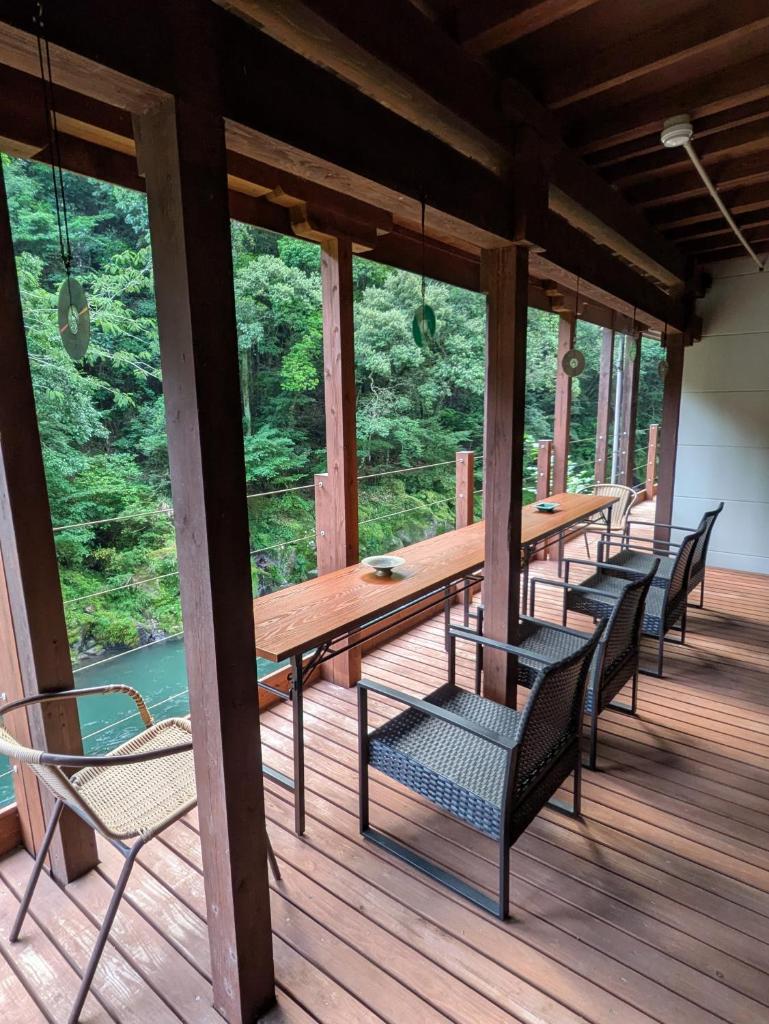 une longue table en bois et des chaises sur une terrasse en bois dans l'établissement 天然温泉旅館 繁花荘せせらぎ, à Kirishima