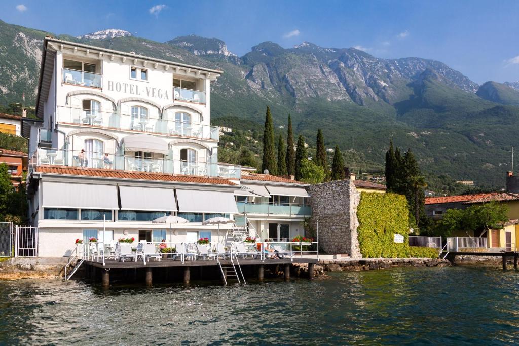 un hôtel sur l'eau avec des montagnes en arrière-plan dans l'établissement Hotel Vega, à Malcesine