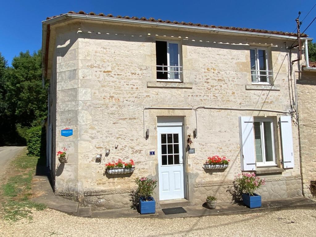 une petite maison en pierre avec une porte blanche et des fleurs dans l'établissement Le Gîte au Coin des Abeilles, à La Caillère