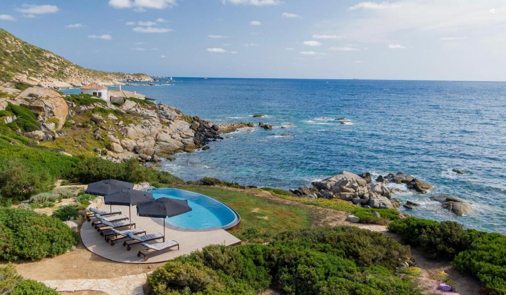 une piscine avec chaises et parasols au bord de l'océan dans l'établissement Pedra - Seaside & pool villa in wild Mediterranean, à San Stèfano