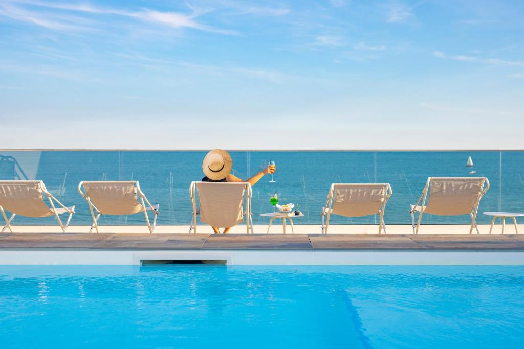 une personne assise dans une chaise à côté d'une piscine dans l'établissement Hotel Ariston, à Caorle