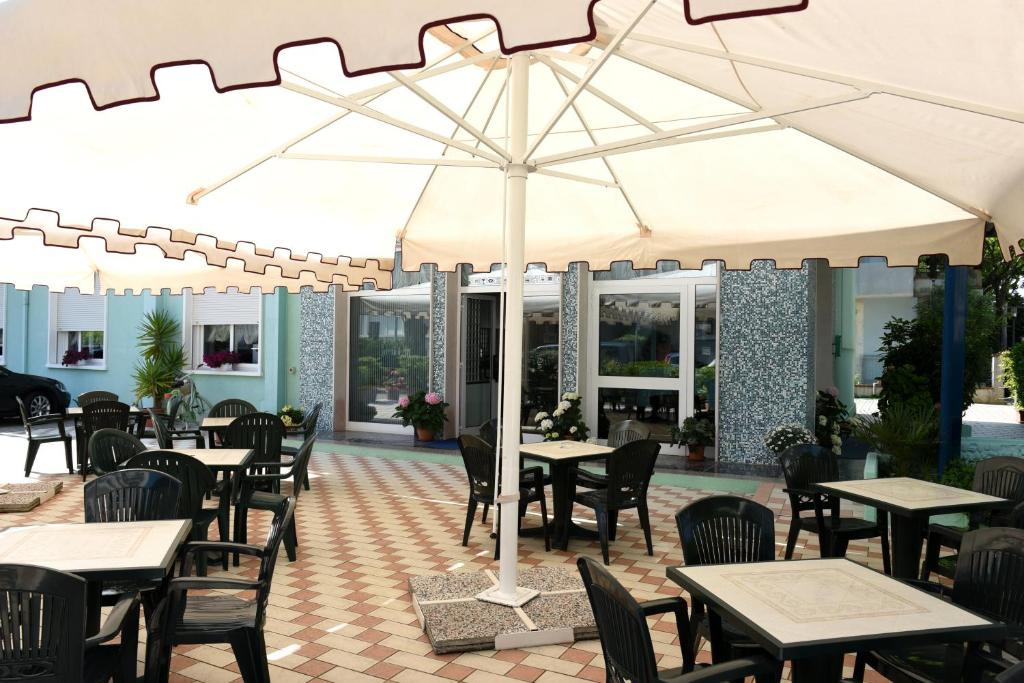 un patio extérieur avec tables, chaises et un parasol dans l'établissement Hotel Savoia, à Lido di Jesolo