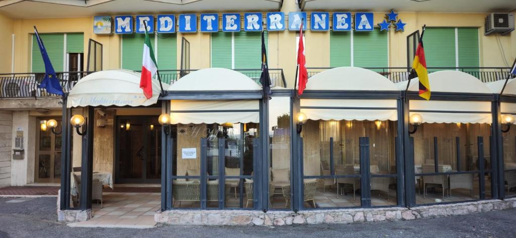 un restaurant avec des drapeaux devant un bâtiment dans l'établissement Hotel Mediterranea, à Loano