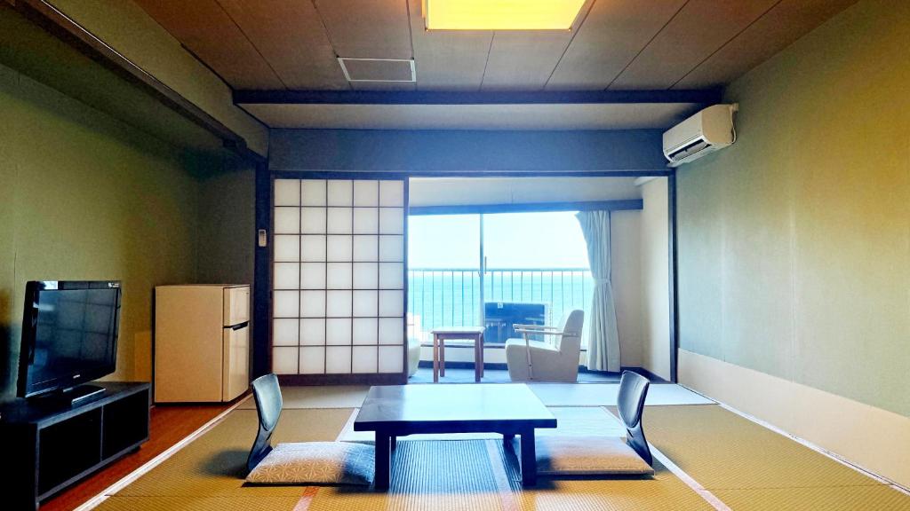 un salon avec une table, des chaises et une télévision dans l'établissement Itoen Hotel Atagawa, à Higashiizu
