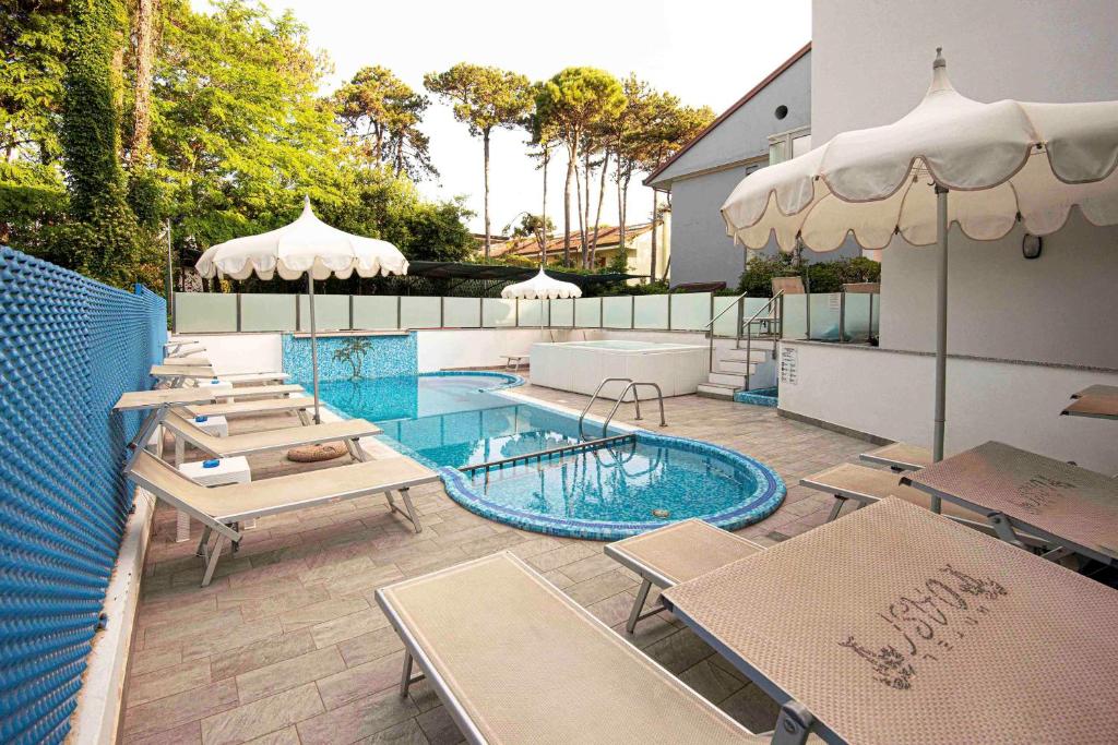 un patio avec piscine, tables et parasols dans l'établissement Hotel Oasi, à Lignano Sabbiadoro