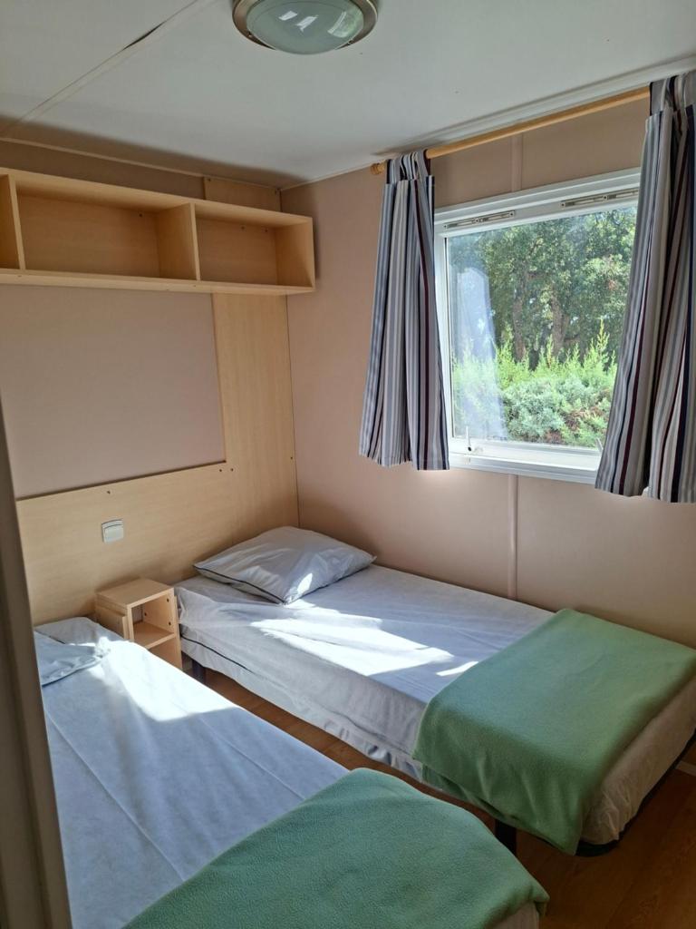 deux lits dans une petite pièce avec une fenêtre dans l'établissement Camping Des Mimosas, à Argelès-sur-Mer