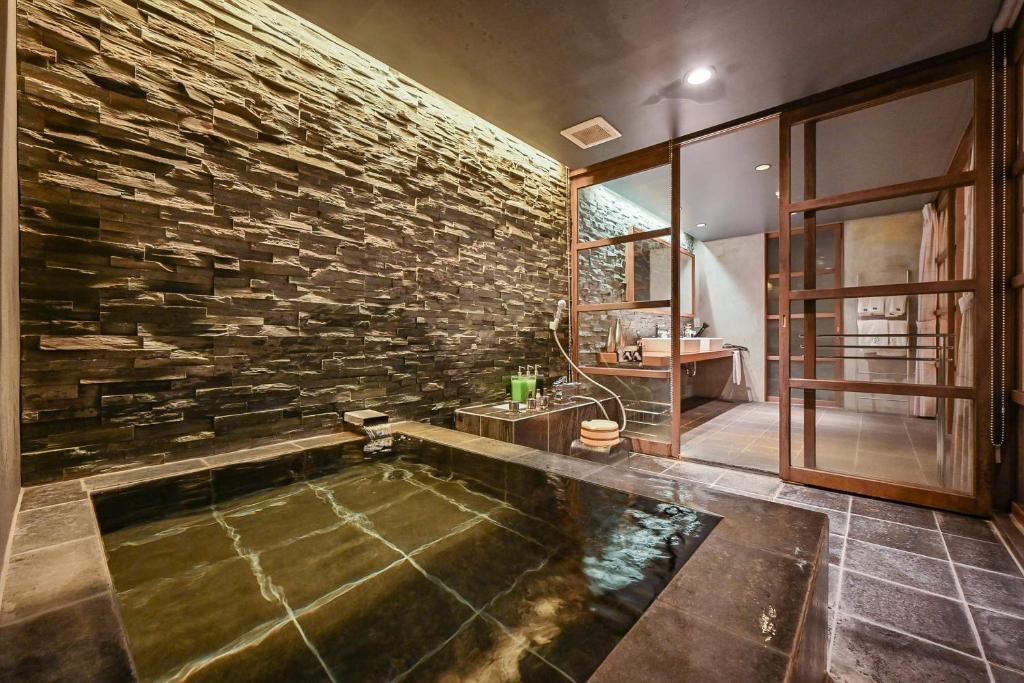 La salle de bains est pourvue d'une grande baignoire avec un mur en pierre. dans l'établissement Ryokan Yoshidaya, à Ureshino