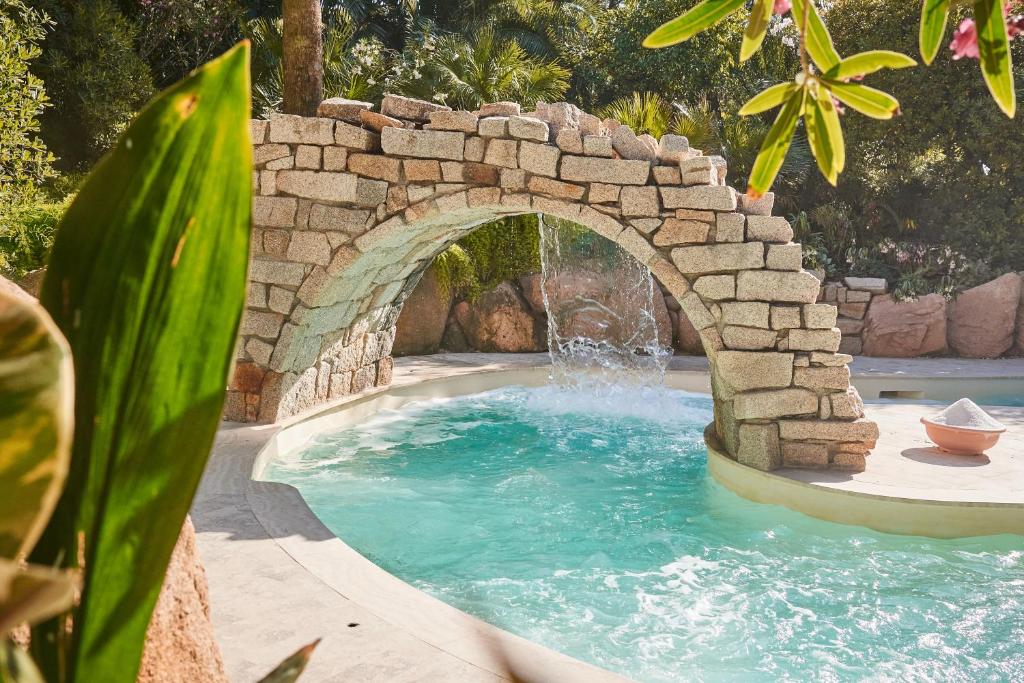 une piscine avec un pont de pierre et une fontaine dans l'établissement Forte Village Resort - Le Palme, à Santa Margherita di Pula
