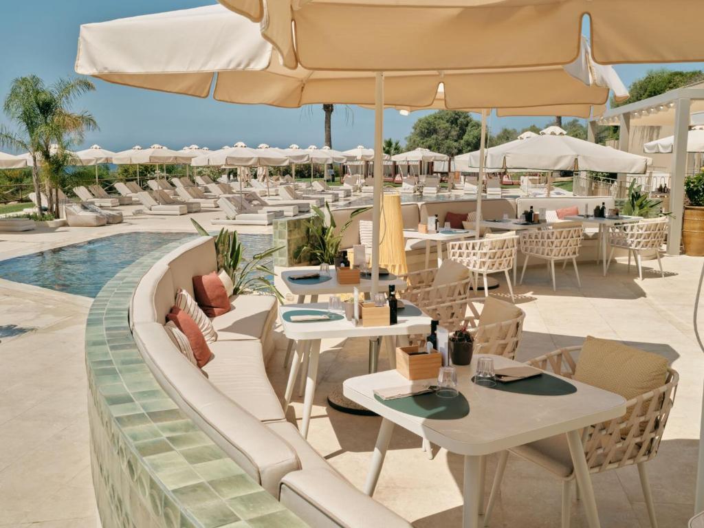 un restaurant avec des tables et des parasols à côté d'une piscine dans l'établissement Mangia's Torre Del Barone Resort & SPA, à Sciacca