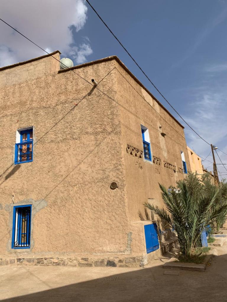 un grand bâtiment en briques avec des fenêtres bleues et un palmier dans l'établissement Chez Youssef, à Merzouga