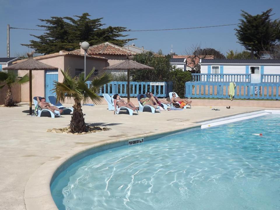 une piscine avec des gens allongés sur des chaises à côté d'une maison dans l'établissement camping le clos fleuri, à Vic-la-Gardiole