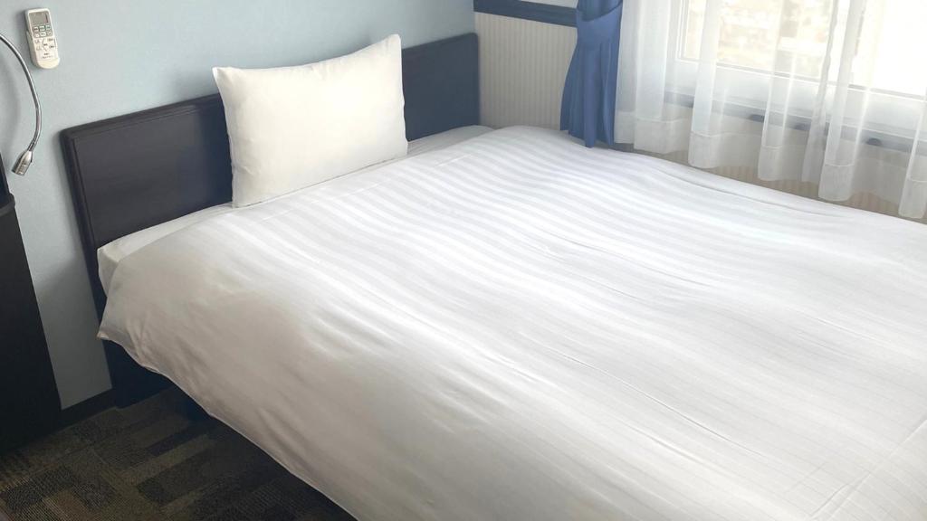 un grand lit blanc dans une chambre avec une fenêtre dans l'établissement Toyoko Inn Saitama Iwatsuki Ekimae, à Saitama