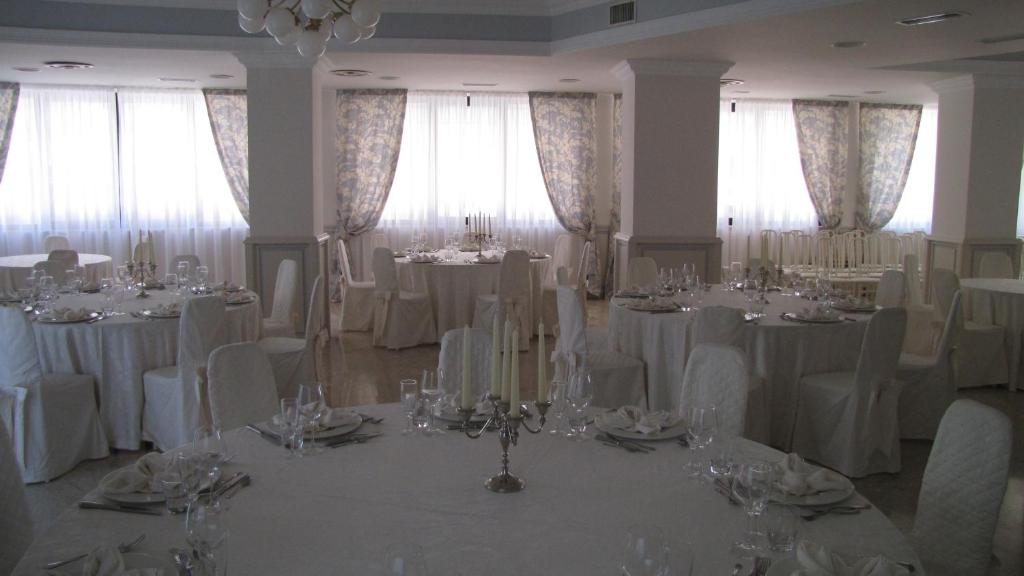 Cette chambre dispose de tables et de chaises blanches ainsi que de fenêtres. dans l'établissement Hotel Lanterna, à Porto San Giorgio