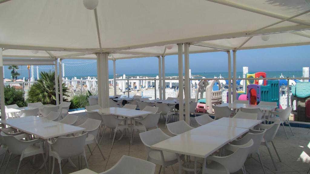 un restaurant avec des tables et des chaises blanches et l'océan dans l'établissement Hotel Lanterna, à Porto San Giorgio