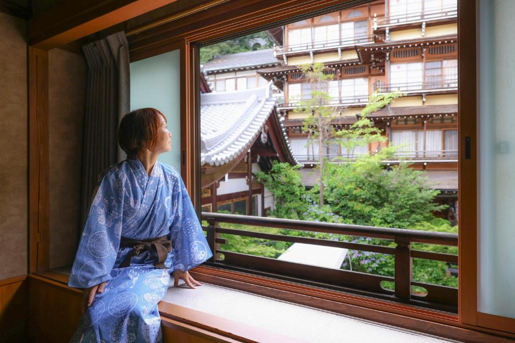 une femme en kimono qui regarde par une fenêtre dans l'établissement Ikariya Ryokan, à Yamanouchi