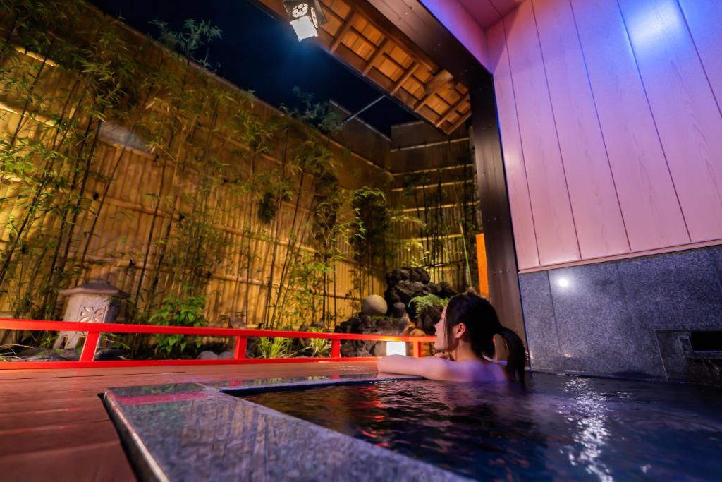 une femme dans un jacuzzi dans un immeuble dans l'établissement 熱海温泉 法悦 旅館, à Atami