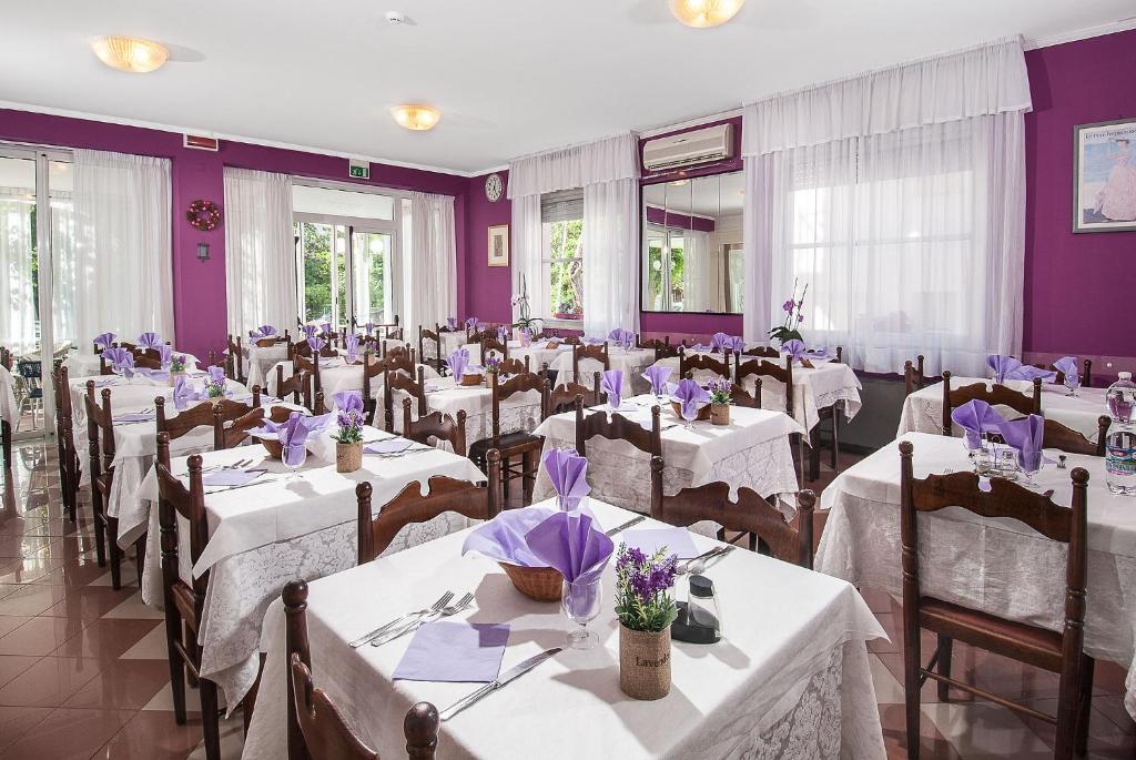 une salle de banquet avec des tables et des chaises blanches et des murs violets dans l'établissement Hotel Cheri, à Rimini