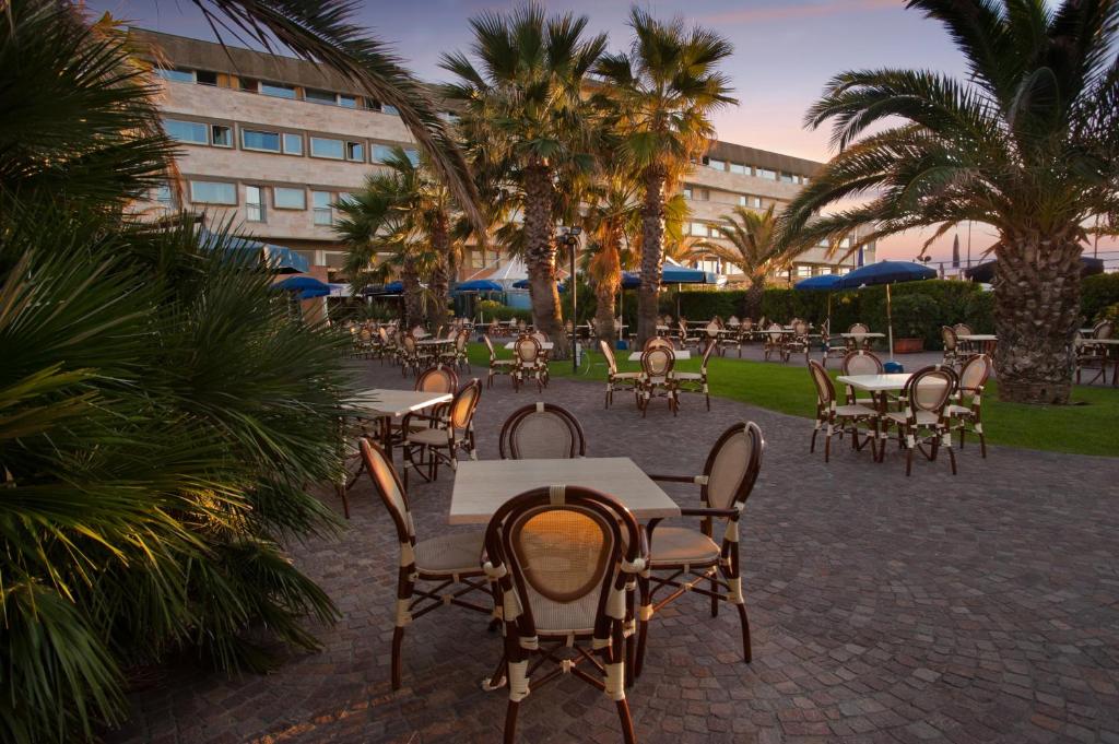d'une terrasse avec des tables, des chaises et des palmiers. dans l'établissement Grand Hotel Continental, à Tirrenia
