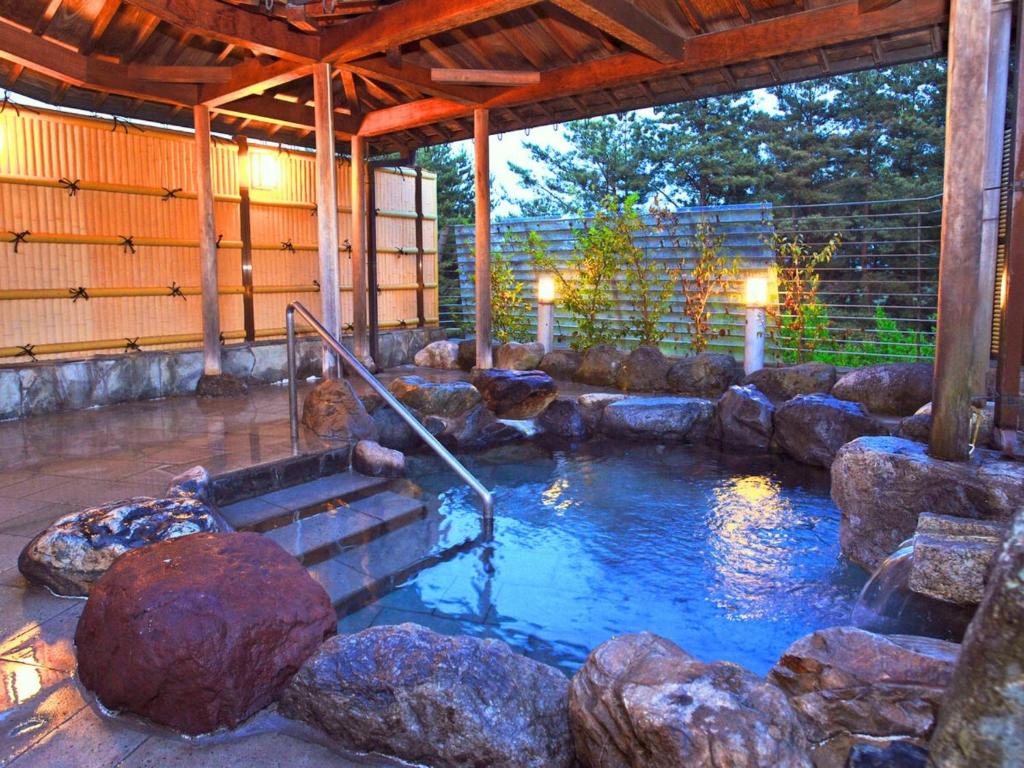 une piscine d'eau avec des rochers dans un bâtiment dans l'établissement Ikoi no mura Notohanto, à Shika