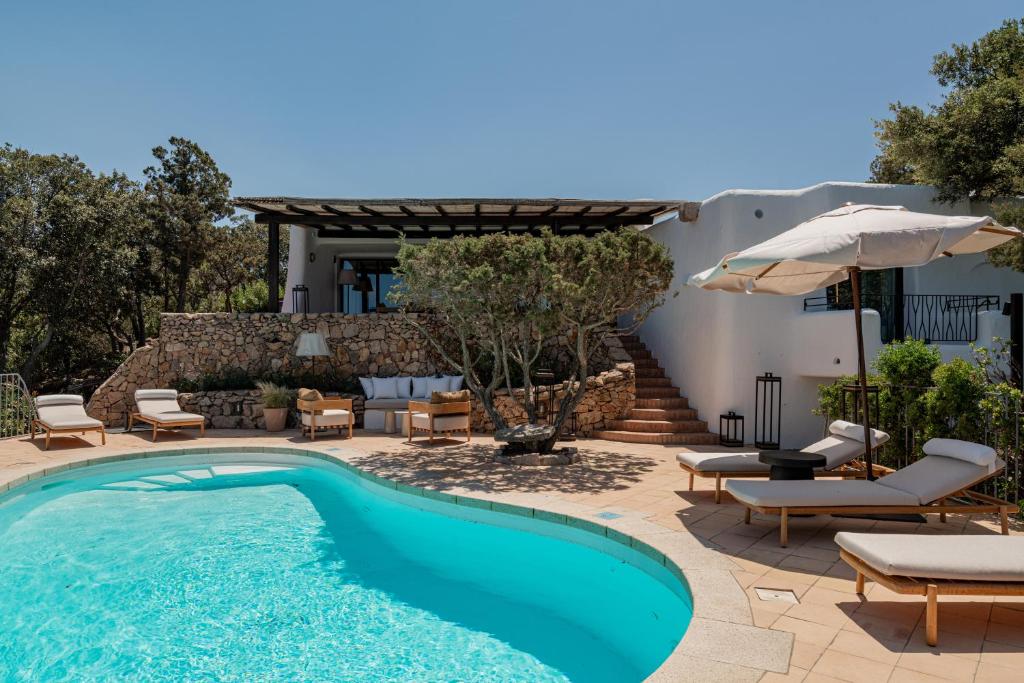 une piscine avec des chaises et un parasol à côté d'une maison dans l'établissement Hotel Pitrizza, Costa Smeralda, à Porto Cervo