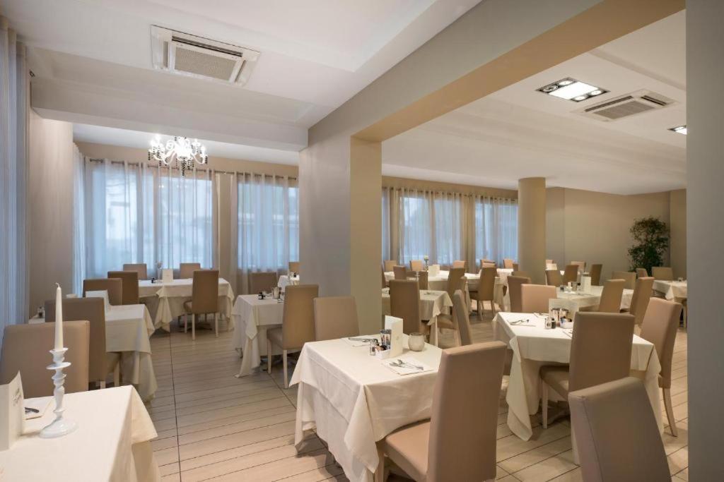 une salle à manger avec des tables et des chaises blanches dans l'établissement Hotel Fiamma & SPA Cesenatico, à Cesenatico