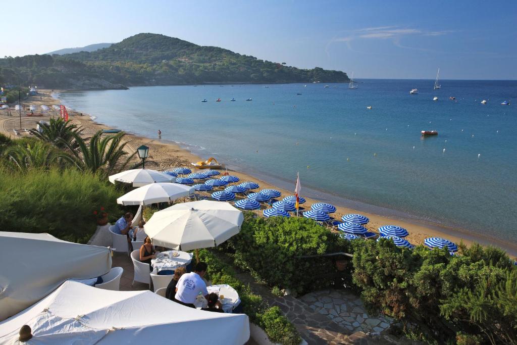 - une plage avec des parasols bleus et blancs et l'océan dans l'établissement Hotel Antares, à Capoliveri