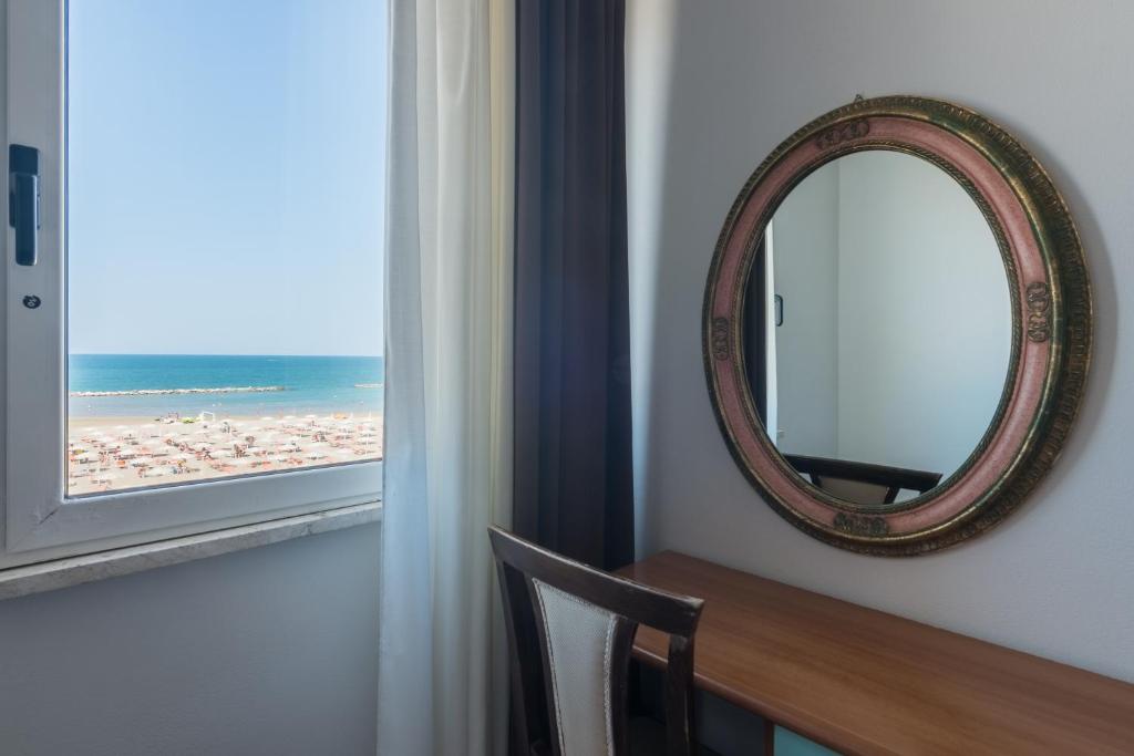 un miroir sur un mur à côté d'une table et d'une fenêtre dans l'établissement Hotel Blumen, à Rimini 98 autres photos