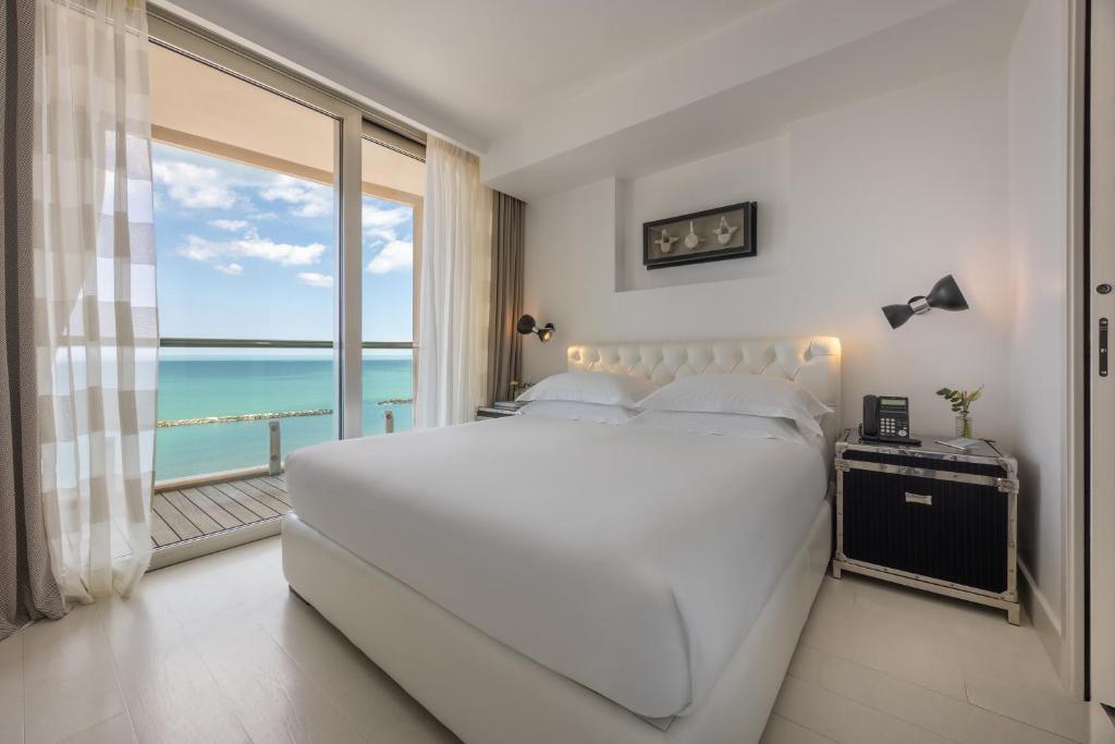 une chambre avec un grand lit blanc et une grande fenêtre dans l'établissement Excelsior Hotel, SPA & Lido - Preferred Hotels & Resorts, à Pesaro