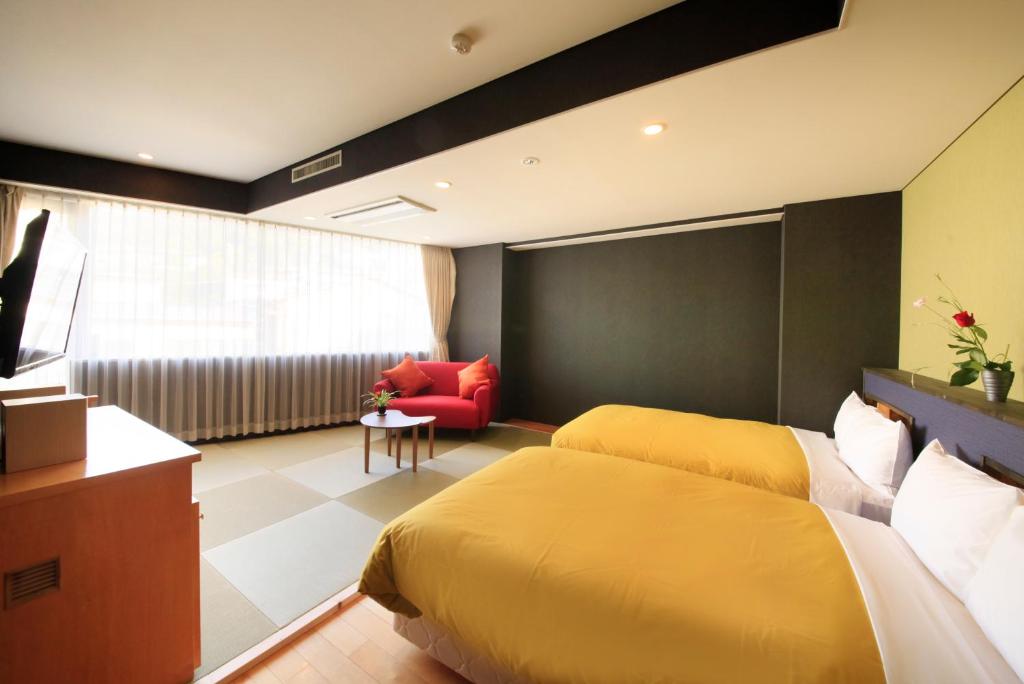 une chambre d'hôtel avec deux lits et une chaise rouge dans l'établissement Atami Tensui, à Atami