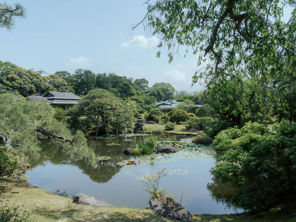 un étang dans un parc avec des arbres et des maisons dans l'établissement Sanyo-so, à Izunokuni