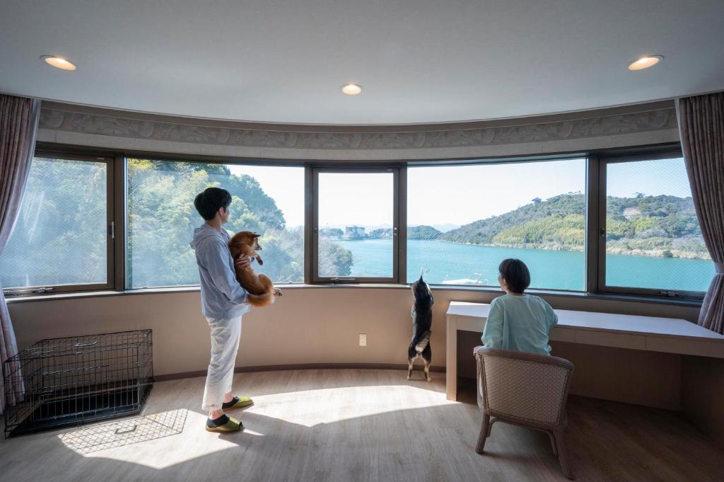 un homme tenant un ours en peluche devant une grande fenêtre dans l'établissement Izumigo Lake Hamana Dog Paradise Hotel, à Hamamatsu
