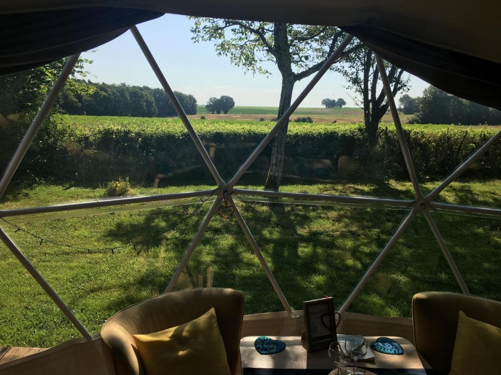 une tente avec une table et des chaises et une vue sur un champ dans l'établissement Le Nid du Tui, à Faverolles