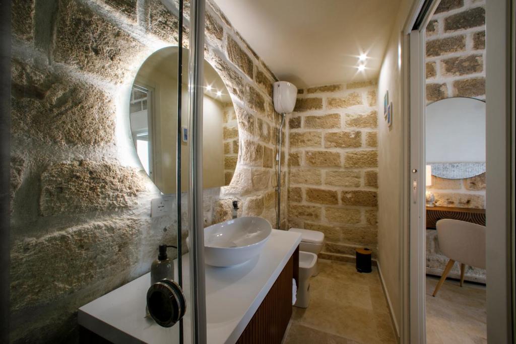 La salle de bains aux murs de pierre est pourvue d'un lavabo et d'un miroir. dans l'établissement La Dimora del Sale - Ville con piscina, à Favignana