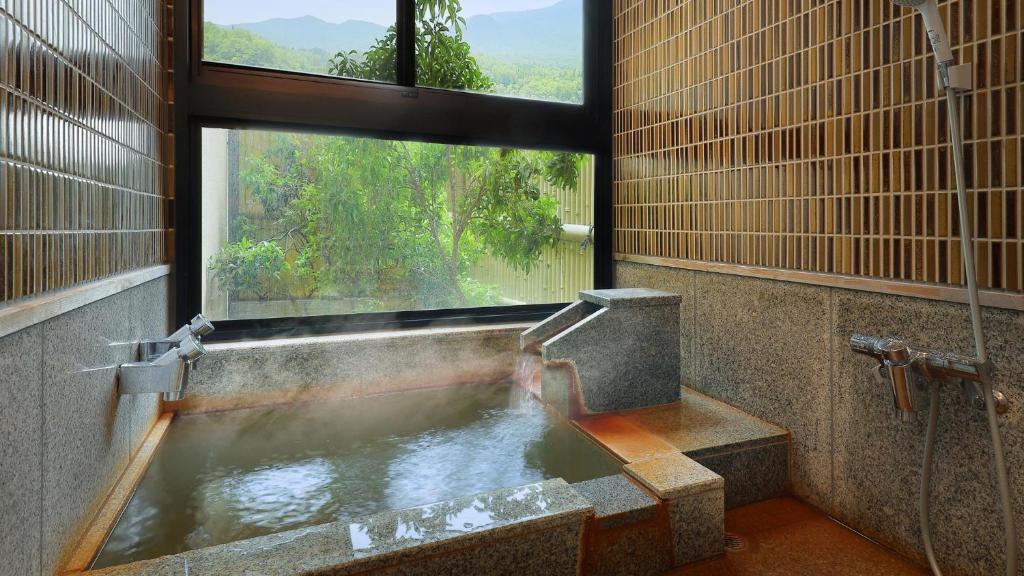 une baignoire avec une grande fenêtre dans une salle de bain dans l'établissement かっぱの宿旅館三治郎, à Zao