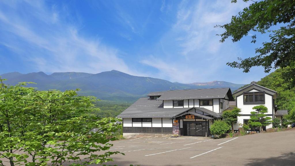 un bâtiment avec un parking avec des montagnes en arrière-plan dans l'établissement かっぱの宿旅館三治郎, à Zao