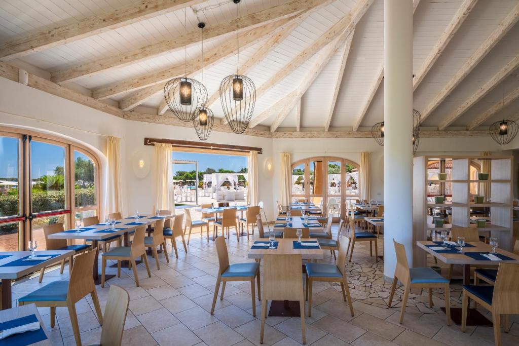 une salle à manger avec tables, chaises et fenêtres dans l'établissement Janna e Sole Resort, à Budoni