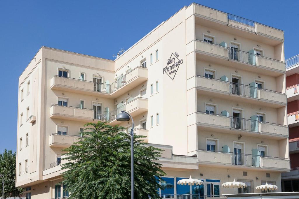 un bâtiment blanc avec un arbre devant lui dans l'établissement Hotel San Francisco Spiaggia, à Rimini