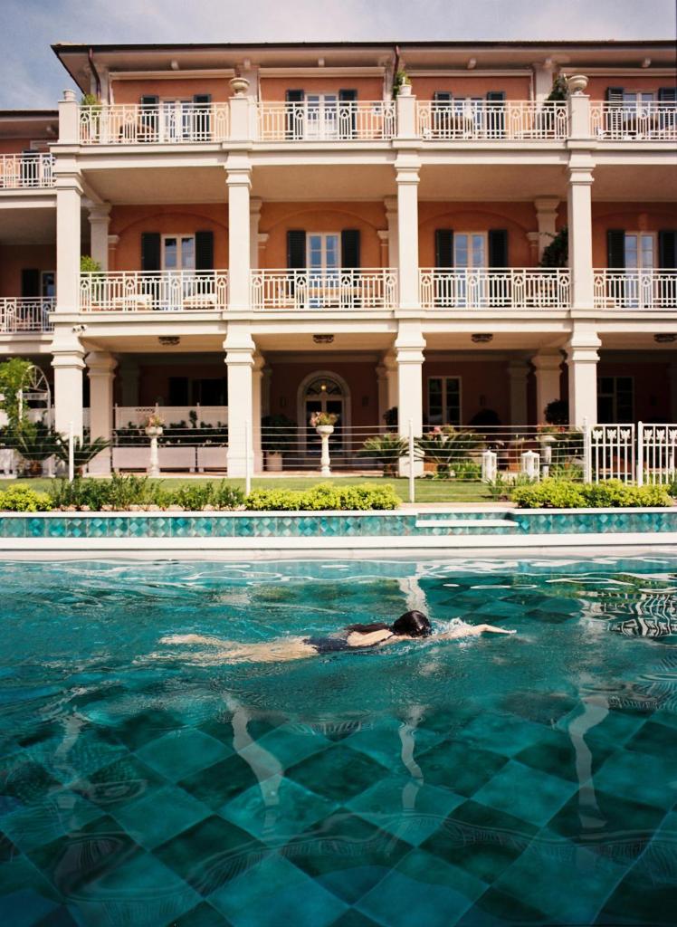une personne se baignant dans une piscine en face d'un bâtiment dans l'établissement Pensione America - Adults only, à Forte dei Marmi