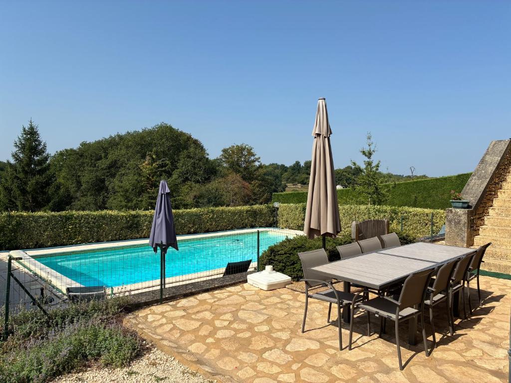 un patio avec une table et des parasols à côté d'une piscine dans l'établissement Gîte de charme à la campagne, à Besse