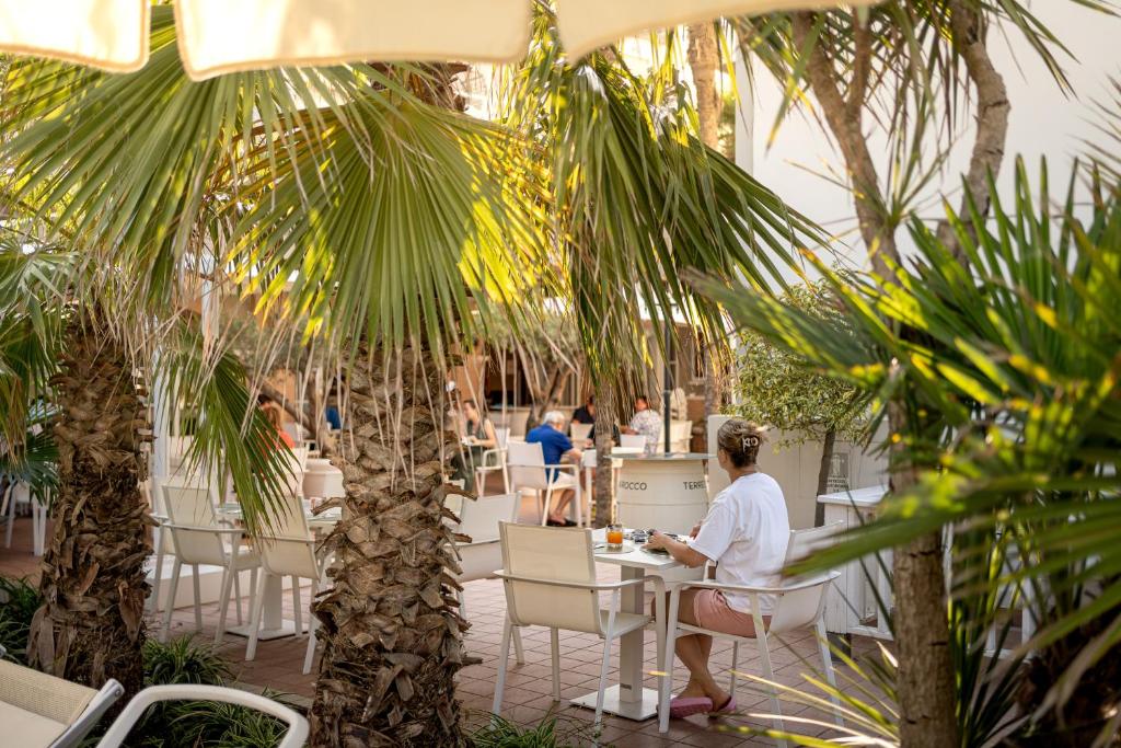 un homme assis à une table dans un restaurant avec des palmiers dans l'établissement Park Hotel Pineta Boutique Hotel, à Caorle