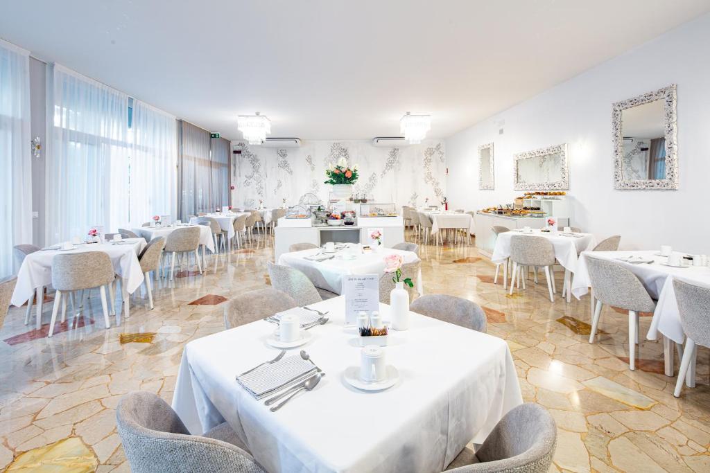 une salle à manger avec des tables et des chaises blanches dans l'établissement Hotel Centrale, à Lignano Sabbiadoro