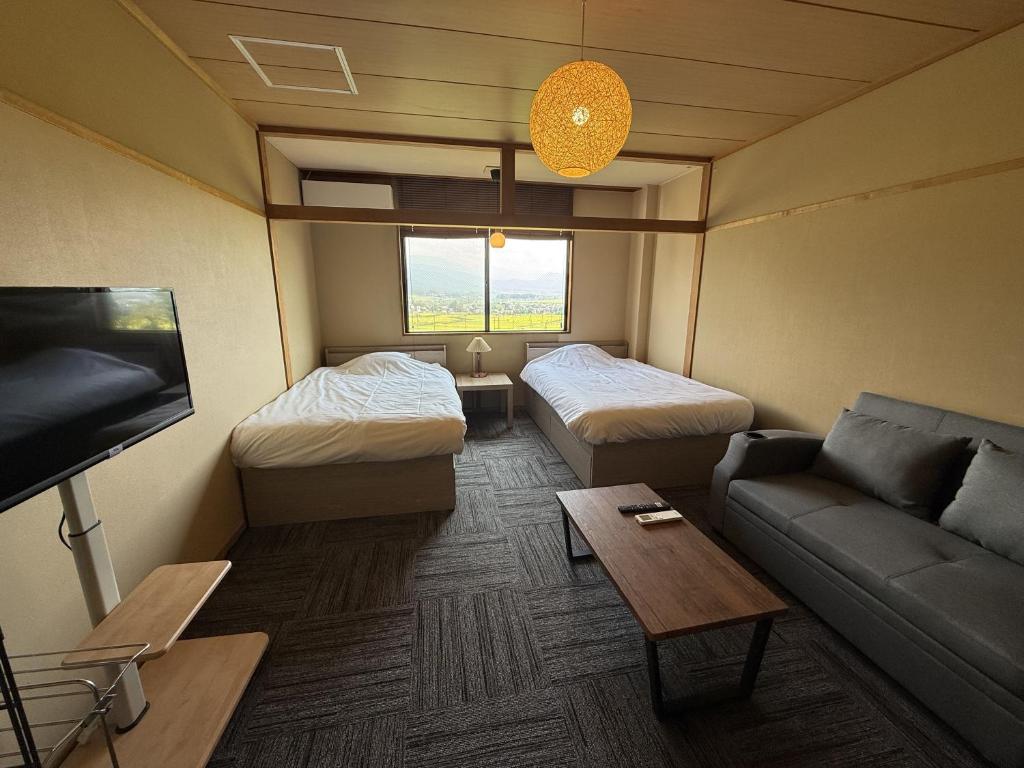 Cette chambre comprend deux lits, un canapé et une télévision. dans l'établissement Togari Onsen Alpen Plaza, à Iiyama