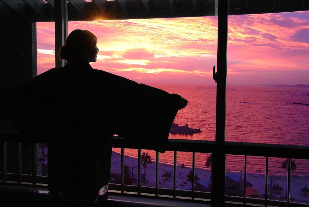 un homme qui regarde par une fenêtre sur l'océan dans l'établissement Hotel Sanrakuso, à Shirahama