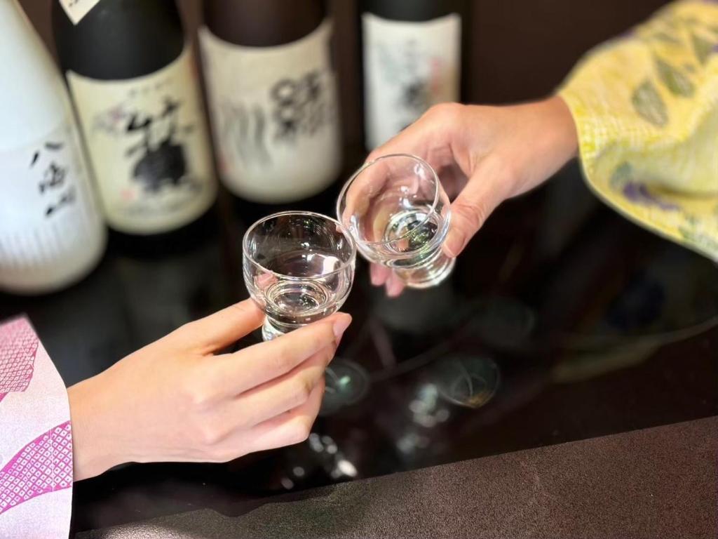deux personnes tenant des verres à vin devant des bouteilles de vin dans l'établissement Kutsurogian, à Minami Uonuma