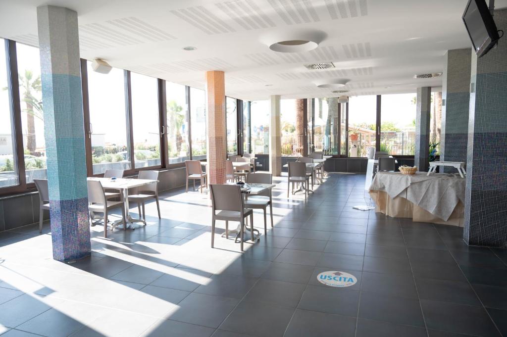 une salle à manger avec tables, chaises et fenêtres dans l'établissement Hotel Graziella, à Martinsicuro
