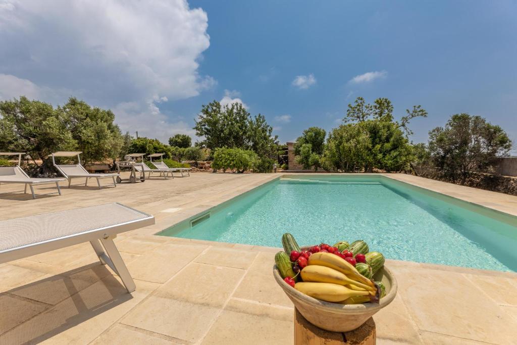 un bol de fruits et légumes à côté d'une piscine dans l'établissement Trullo la Ficarigna, à Alliste