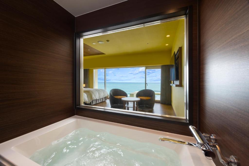 une salle de bain avec une baignoire avec un grand miroir dans l'établissement Kamogawa Grand Hotel, à Kamogawa