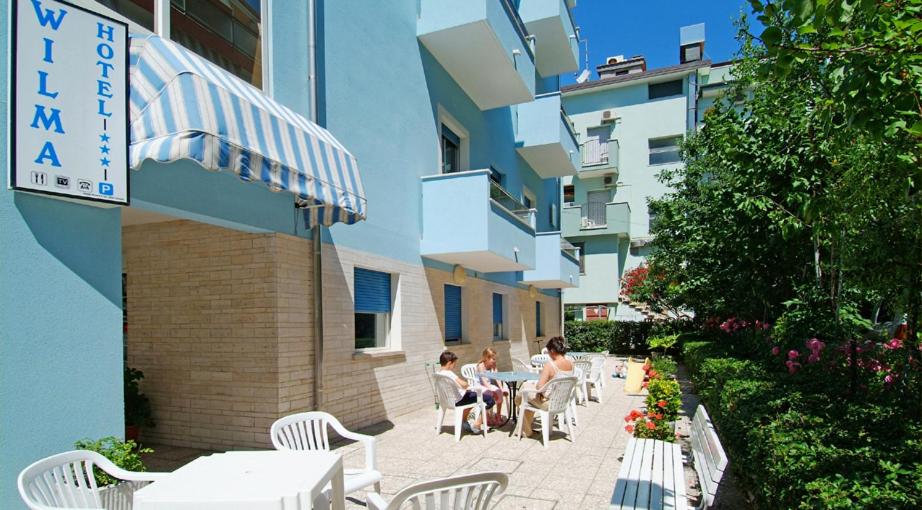 2 personnes assises sur une terrasse à l'extérieur d'un bâtiment dans l'établissement Hotel Wilma, à Rimini
